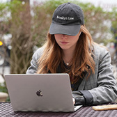 A female student with a Brooklyn Law hat working on a laptop outside.
