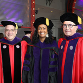 Three people posing for a photo wearing graduation caps and gowns with two men on the right and left and a woman in the middle.