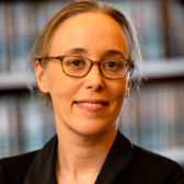 A woman with glasses in front of a bookcase.